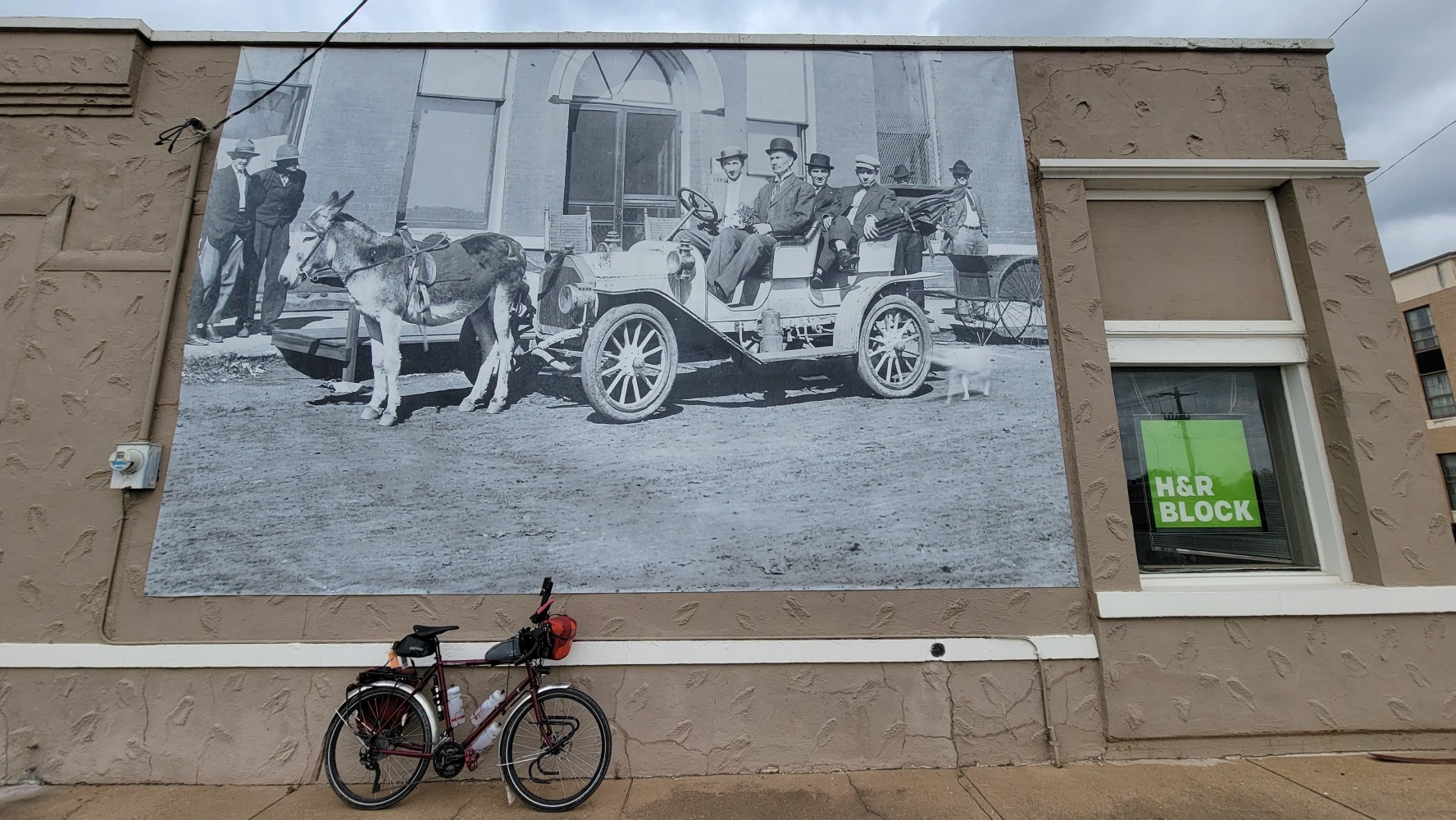 A very stern man at the wheel of a car in this vintage photo on the side of the H&R Block office.